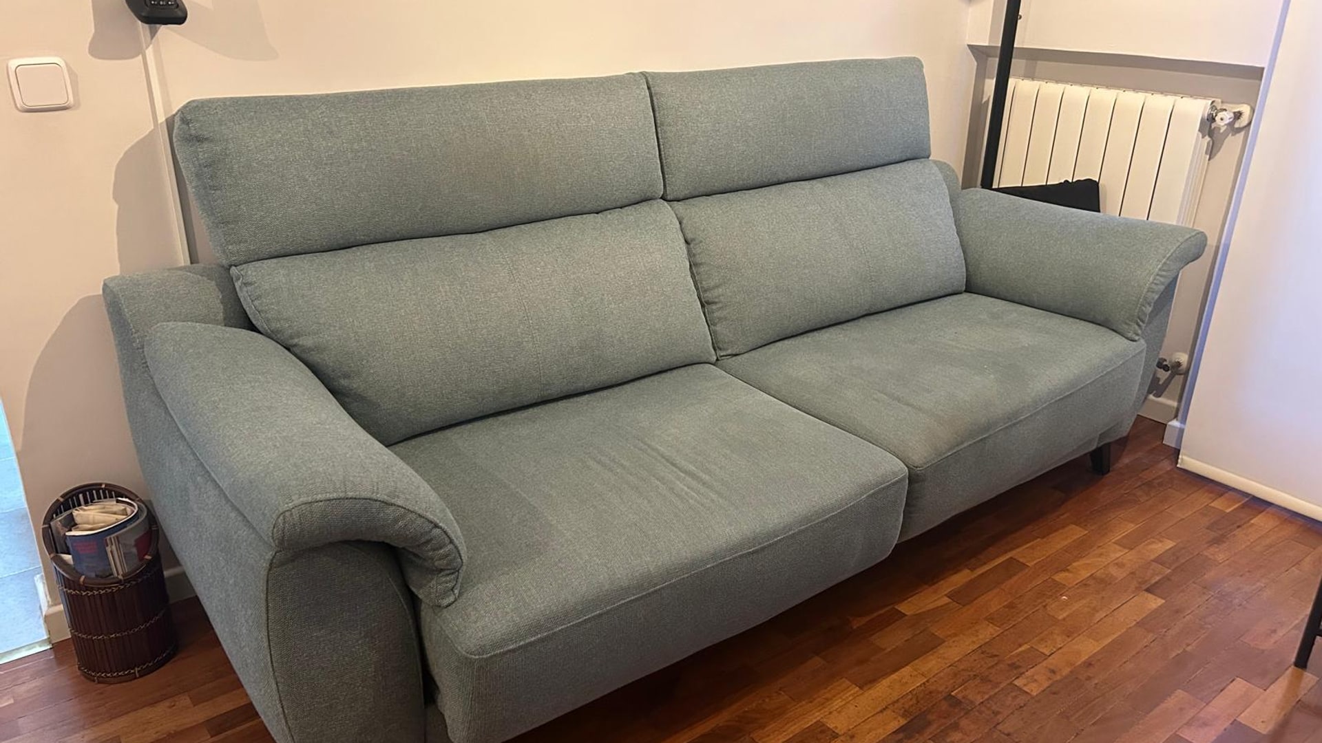 Sofá tapizado en tela sage moderna, ambiente de salón con luz cálida