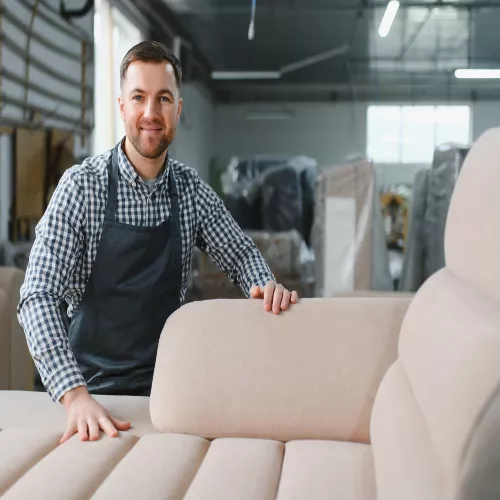 Fabricación de sofas a medida, es un hombre mostrando un sofá terminado. El sofa es Beige clarito y pinta muy cómodo